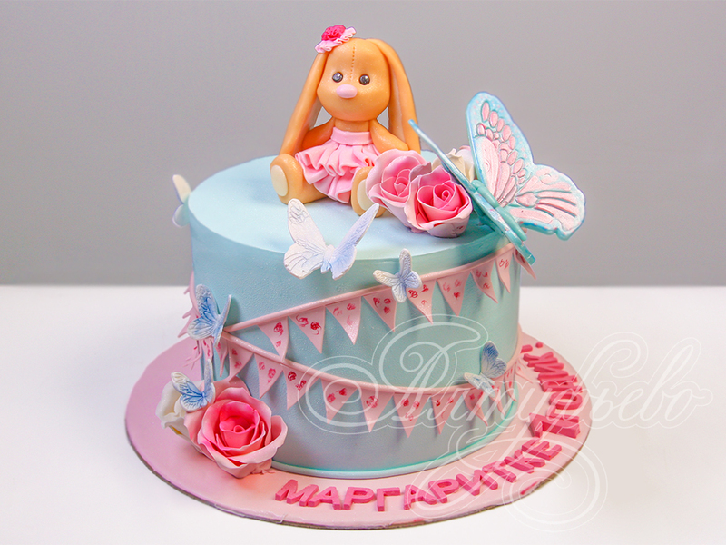 Детский торт девочке на годик голубого цвета с бабочками и фигуркой плюшевого зайчика